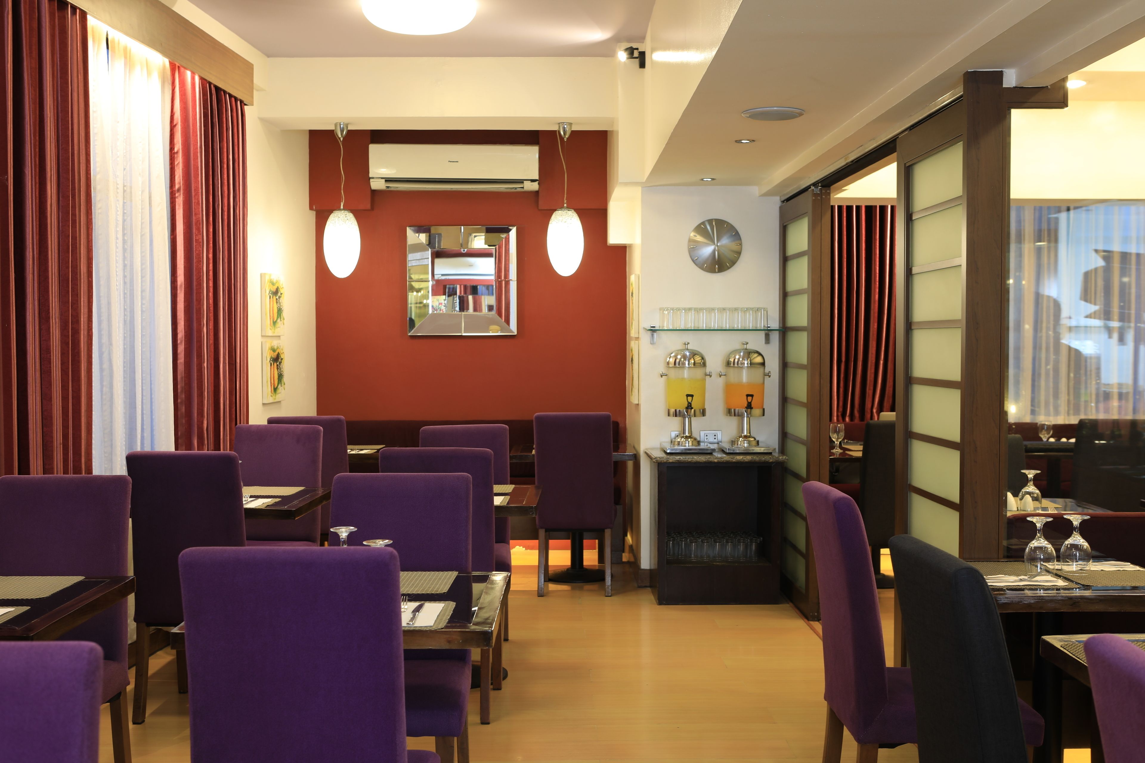 A restaurant with purple chairs, a bar area, and a mirror on the wall.