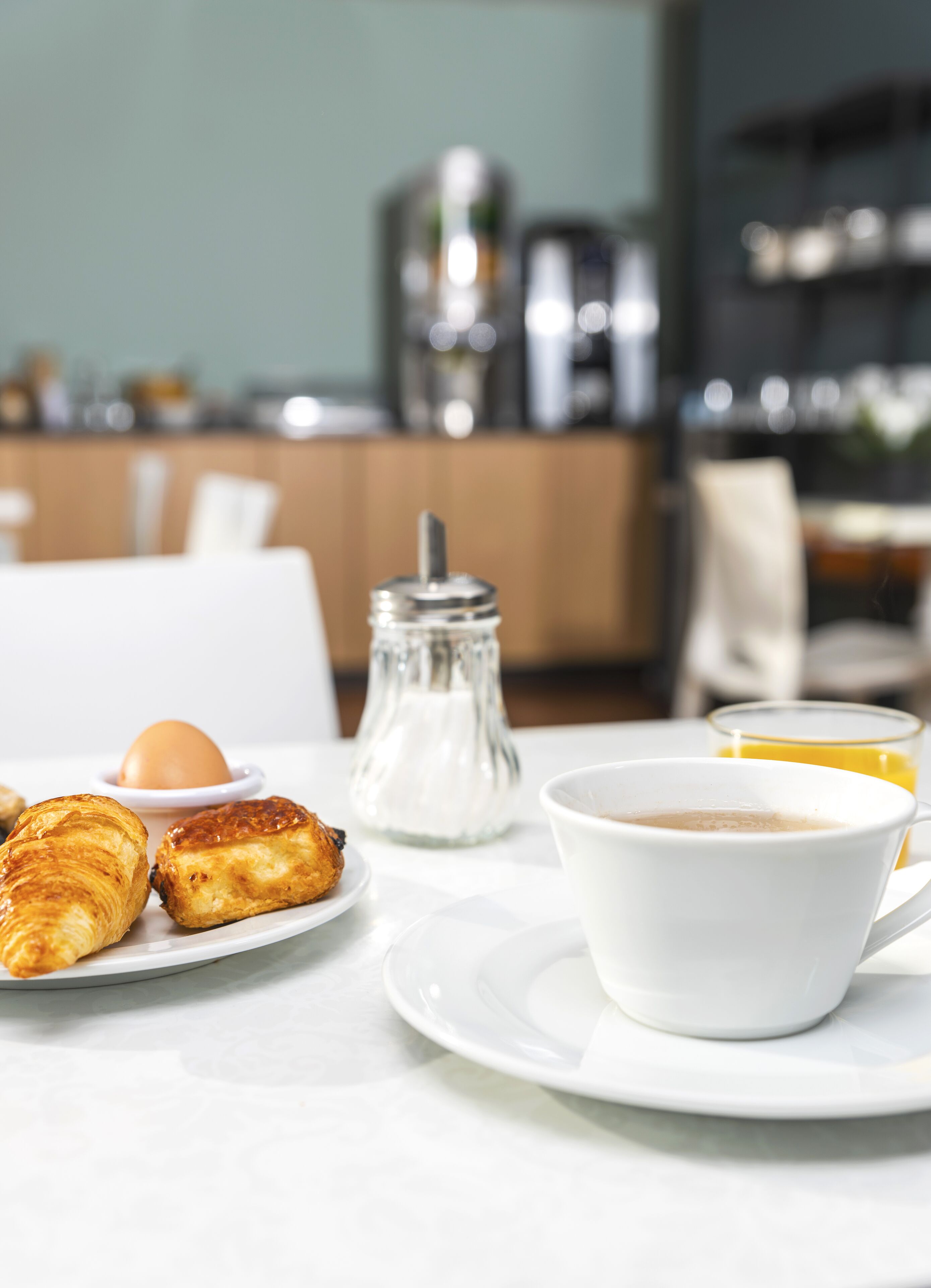 Desayuno con cruasanes, una taza de café, un vaso de zumo de naranja y un salero sobre una mesa blanca.