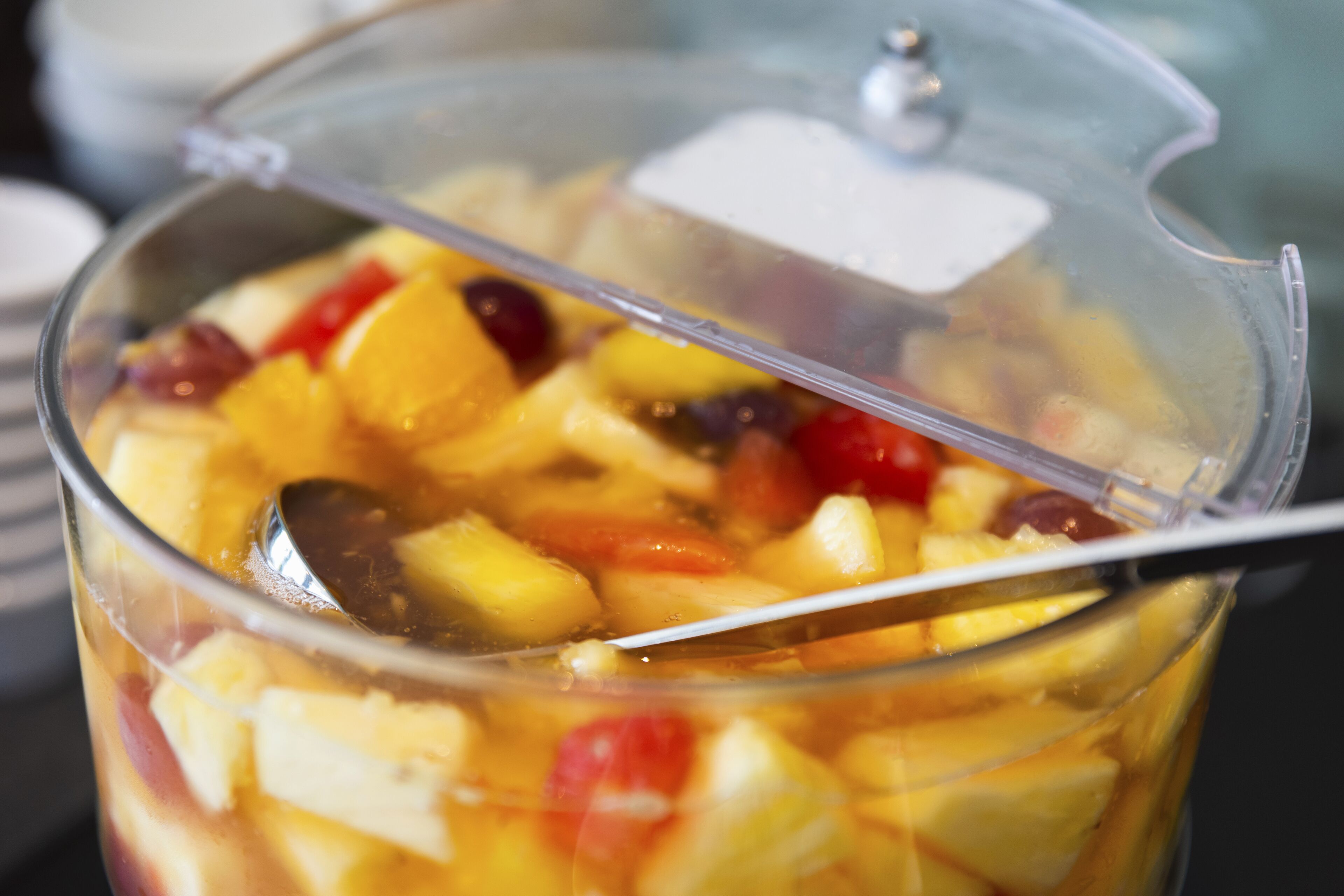 Un recipiente de plástico transparente lleno de frutas cortadas en cubos y una cuchara.