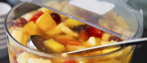 Un recipiente de plástico transparente lleno de frutas cortadas en cubos y una cuchara.