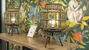 Two wicker lamps on a wooden table with a framed certificate, set against a vibrant mural with birds and foliage. - Ténéo Apparthotel Talence - Centre (Talence)