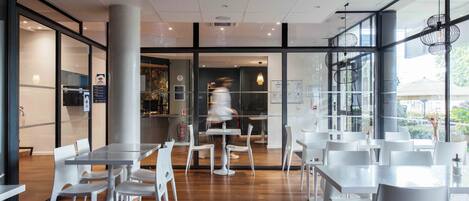 A modern cafe interior with white tables and chairs, a wooden floor, and large windows.