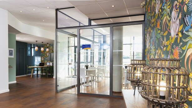 A modern interior with a wooden floor, glass doors leading to a dining area, and a decorative wall with a bird mural. - Ténéo Apparthotel Talence - Centre (Talence)