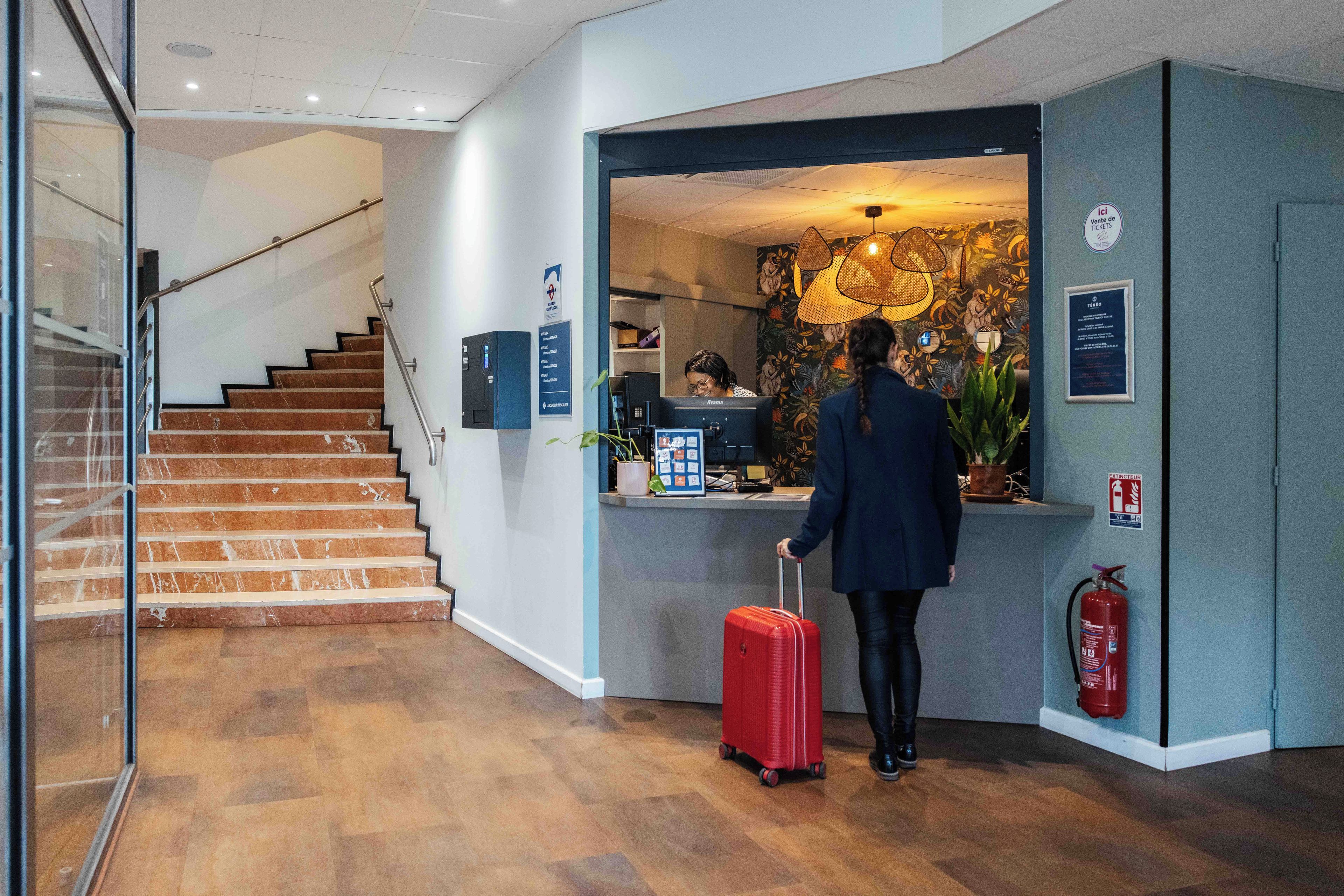 Zona de recepción de un hotel con una escalera, un mostrador de recepción y un extintor.