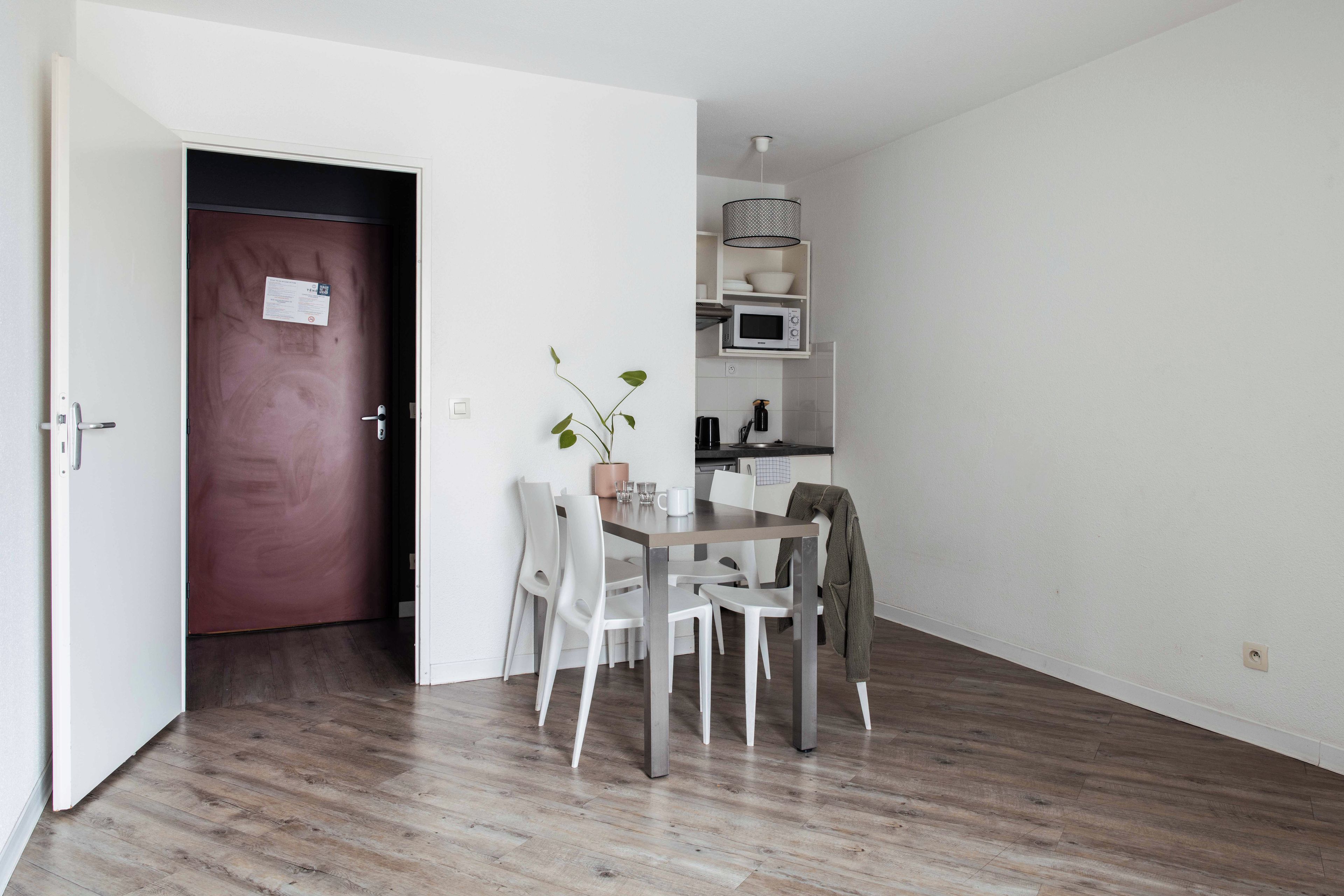 Una habitación con una mesa de comedor, sillas, un microondas y una puerta con un cartel.