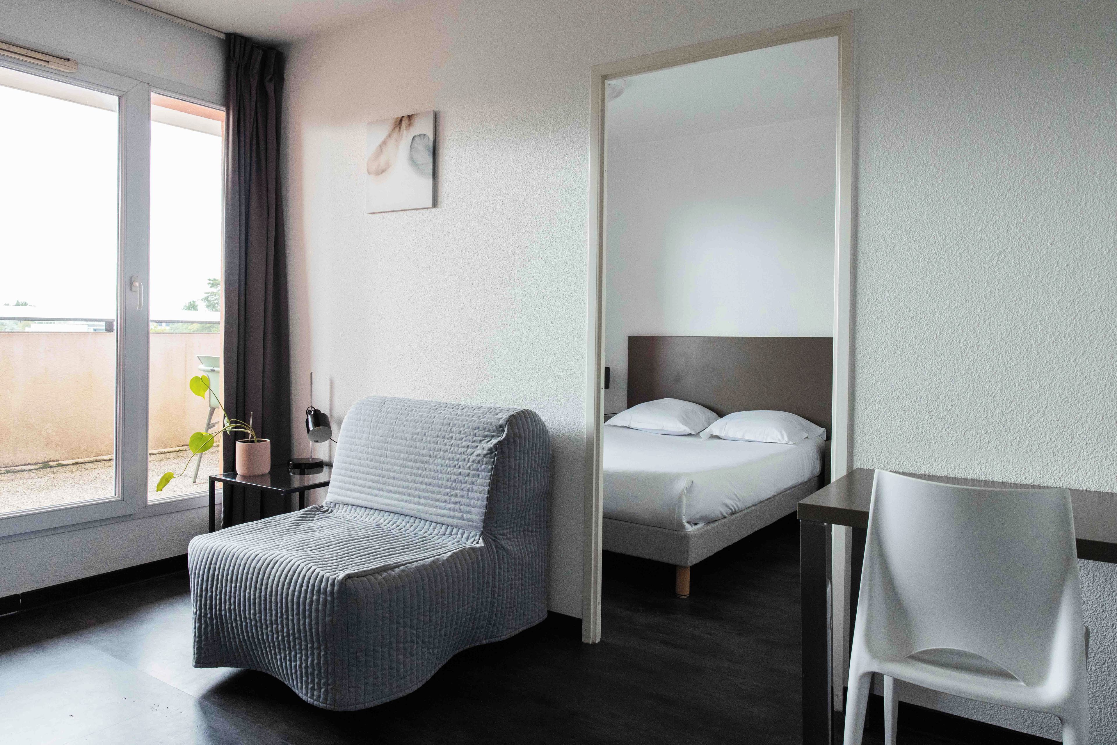 Ein Hotelzimmer mit Bett, Stuhl, Schreibtisch und Blick ins Freie.