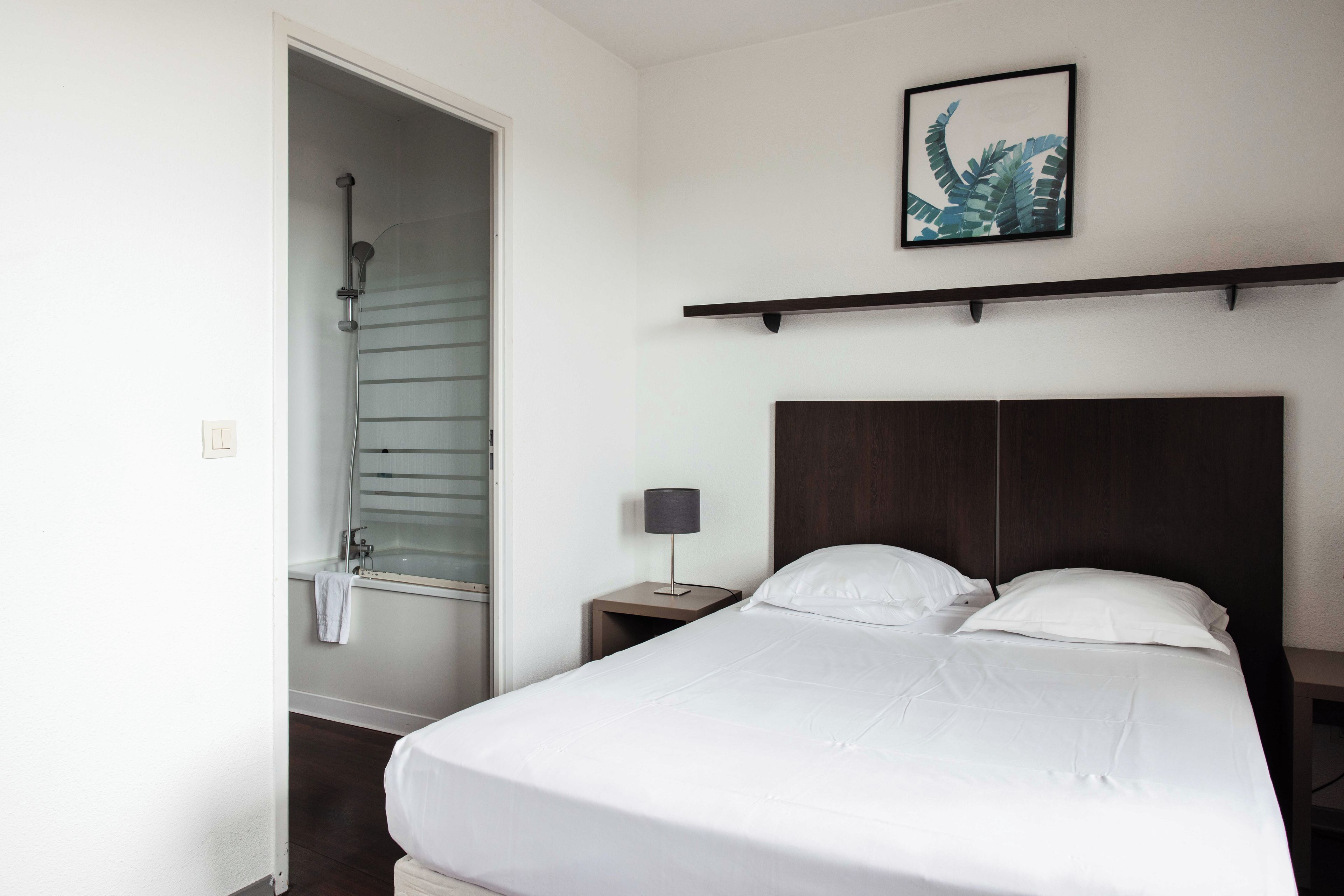 A hotel room with a bed, a nightstand, a lamp, a framed picture on the wall, and a shower.