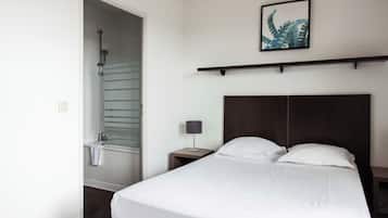 A hotel room with a bed, a nightstand, a lamp, a framed picture on the wall, and a shower.