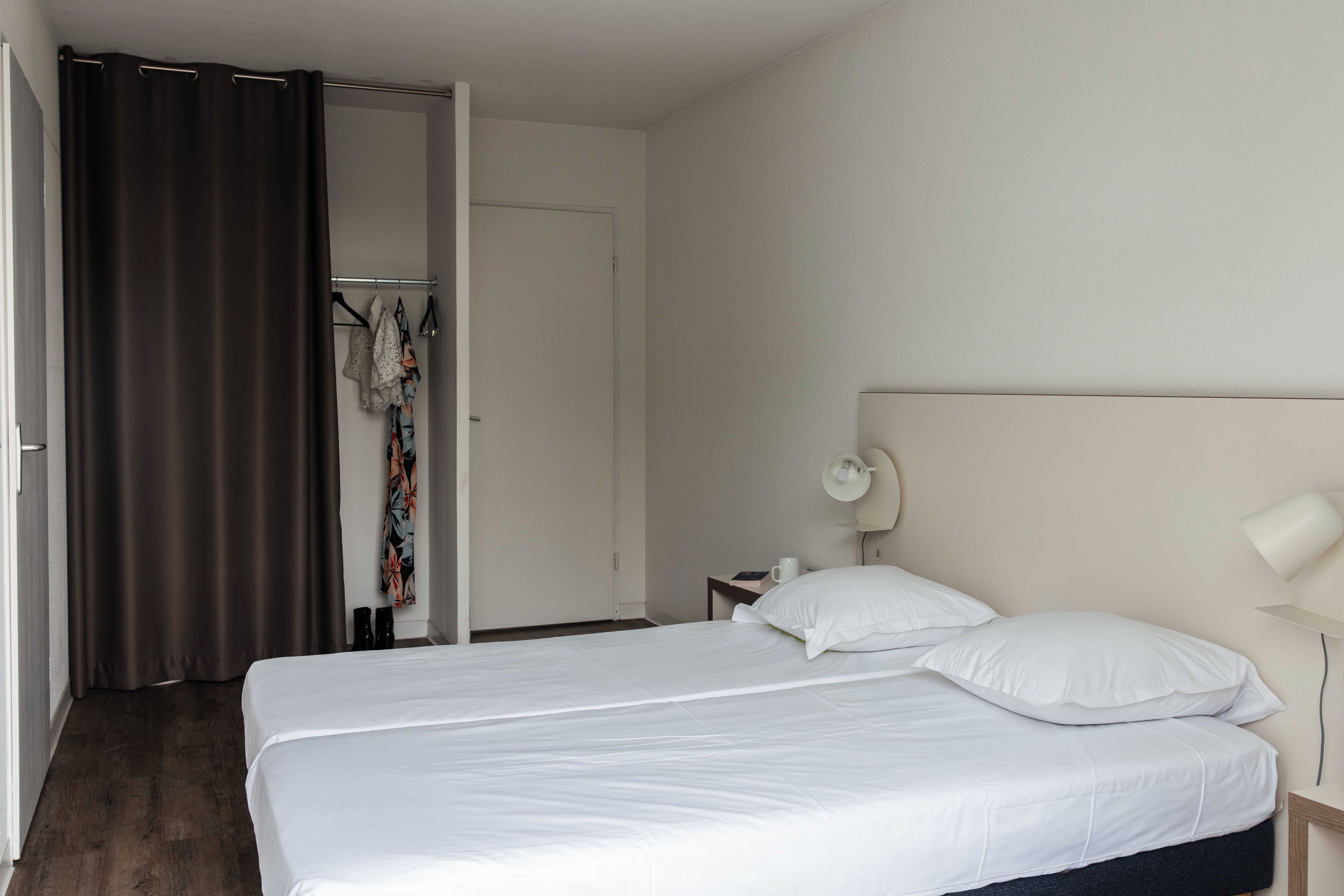Ein Hotelzimmer mit einem Doppelbett, einem Nachttisch mit Lampe und einem Kleiderschrank mit Kleidung.