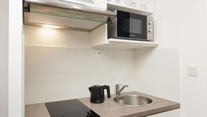 A compact kitchenette with a microwave, kettle, and sink. - Ténéo Apparthotel Talence - Centre (Talence)