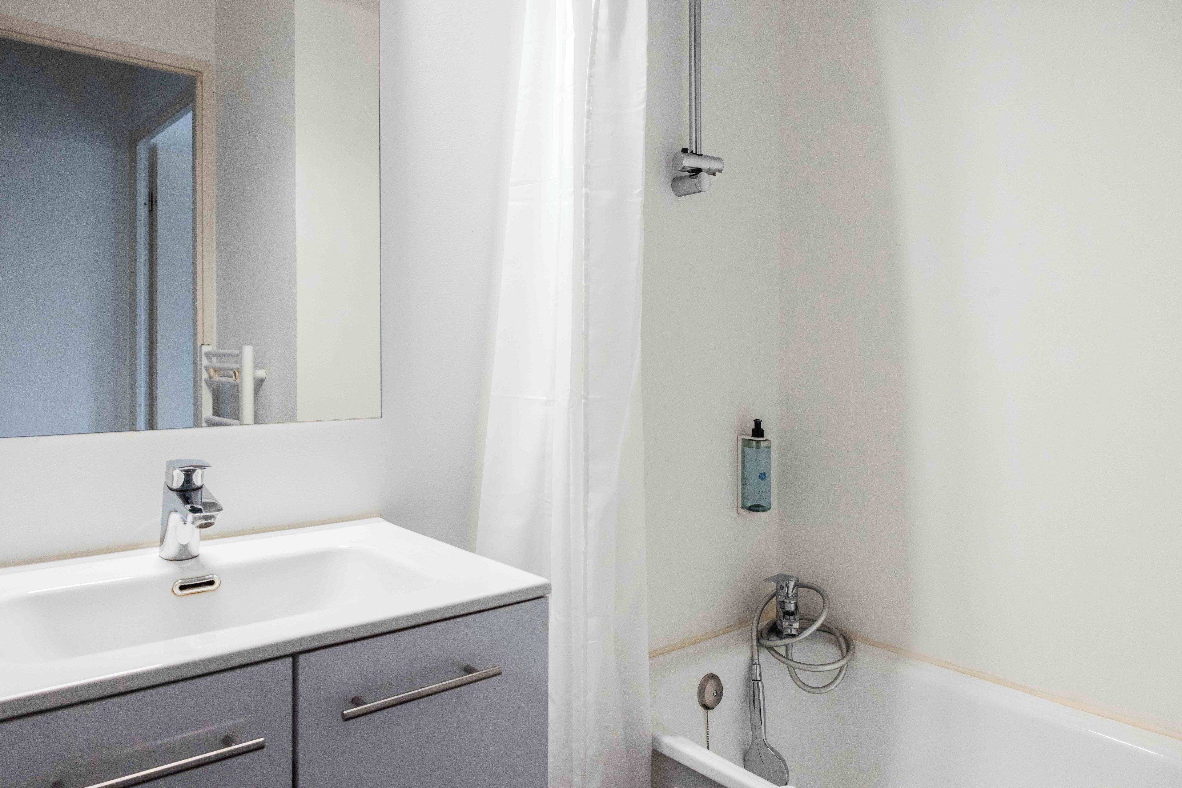 Un baño con lavamanos blanco, espejo, ducha y perchero para toallas.