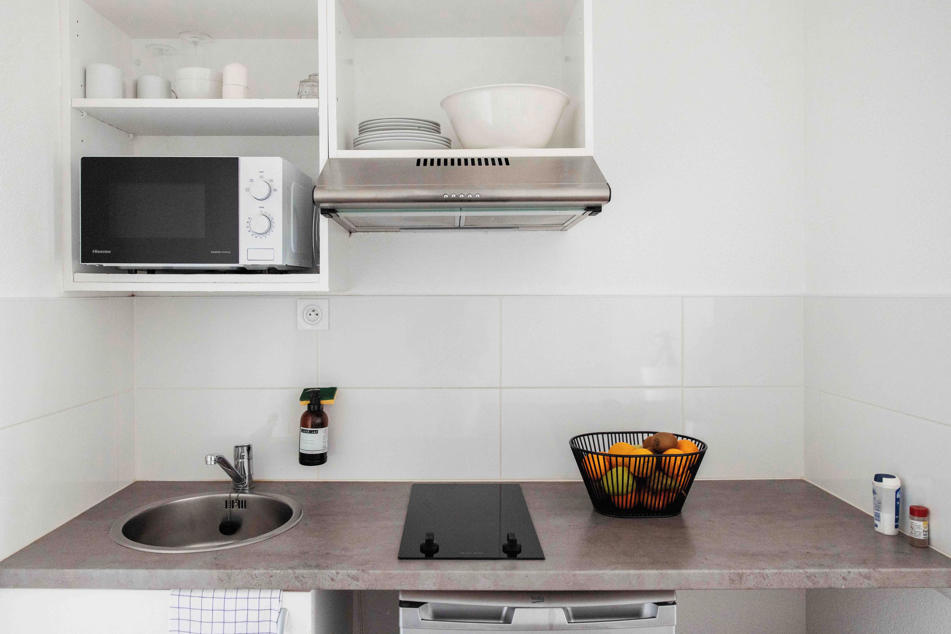 Una cocina con microondas, campana extractora de acero inoxidable, fregadero y encimera con una cesta de fruta.