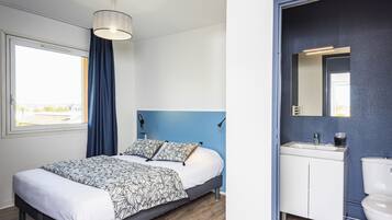 A modern bedroom with a bed, a window with curtains, and a bathroom with a sink and toilet.