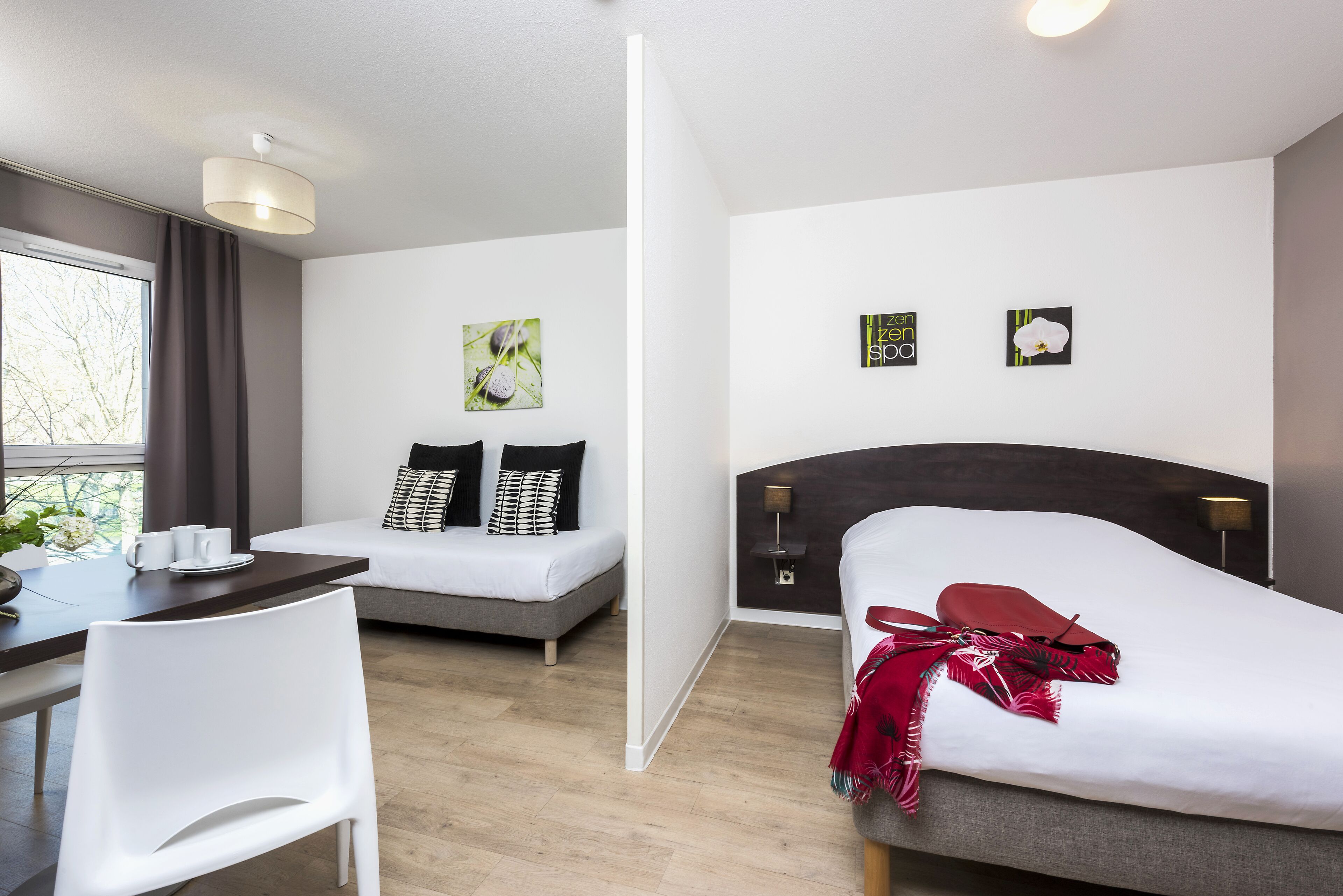 A modern hotel room with a bed, a sofa, a dining table with chairs, and artwork on the walls.