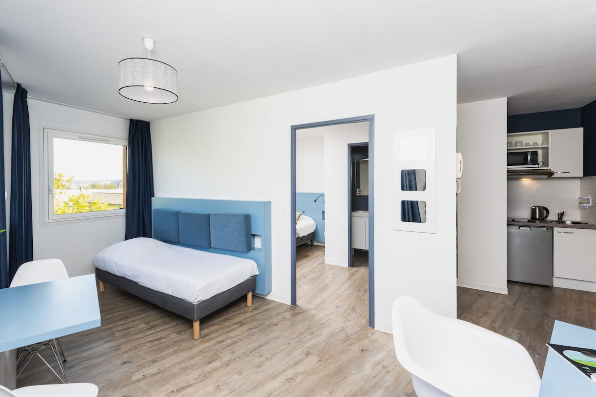 A modern hotel room with a bed, a desk, and a view of the outdoors.