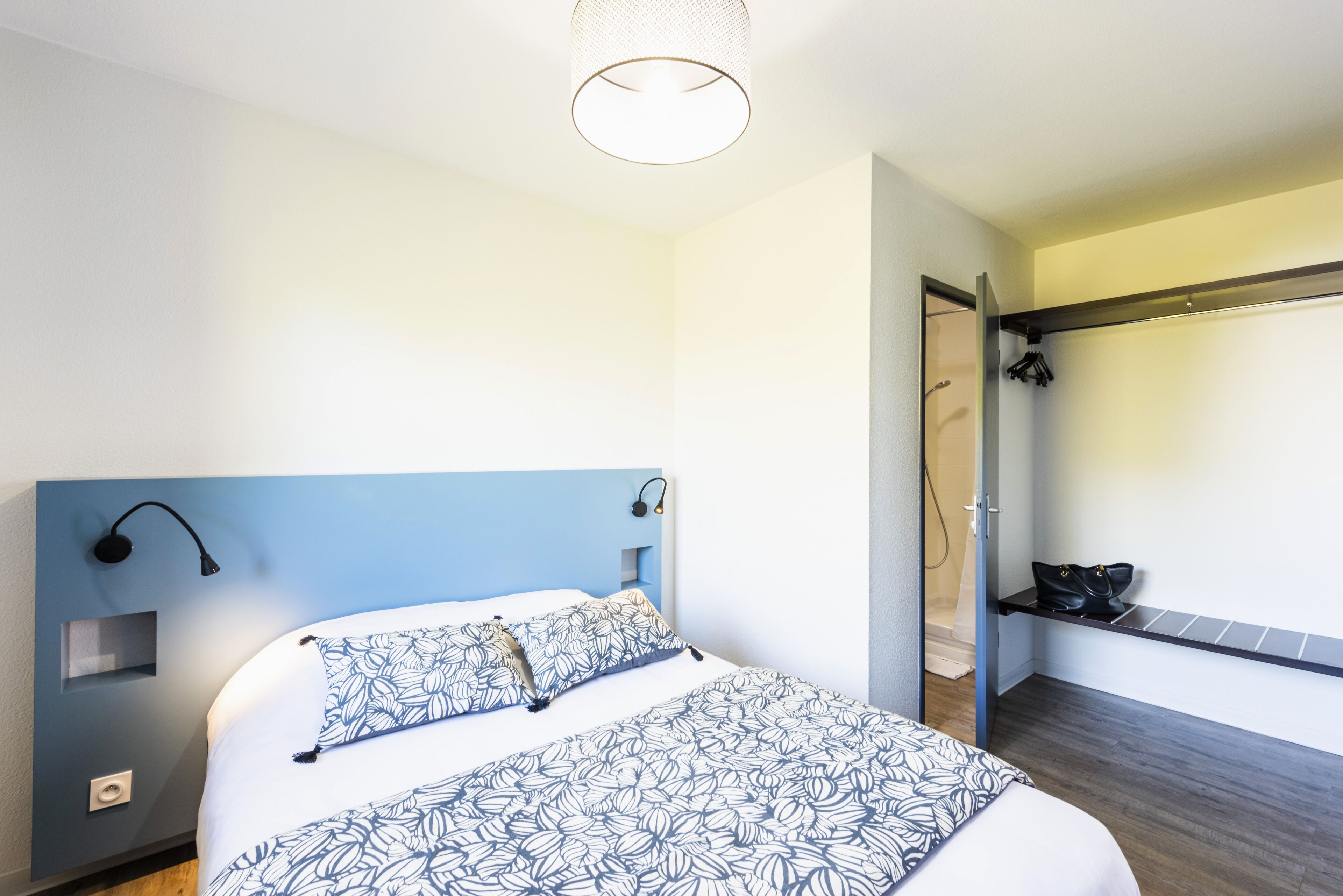 Ein Schlafzimmer mit einem Bett, einem Nachttisch, einer Wandlampe und einem Schuhregal.