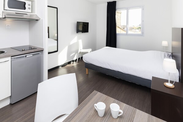 Una habitación de hotel moderna con una cama, un escritorio con una silla, un microondas, un televisor y una ventana con cortinas.