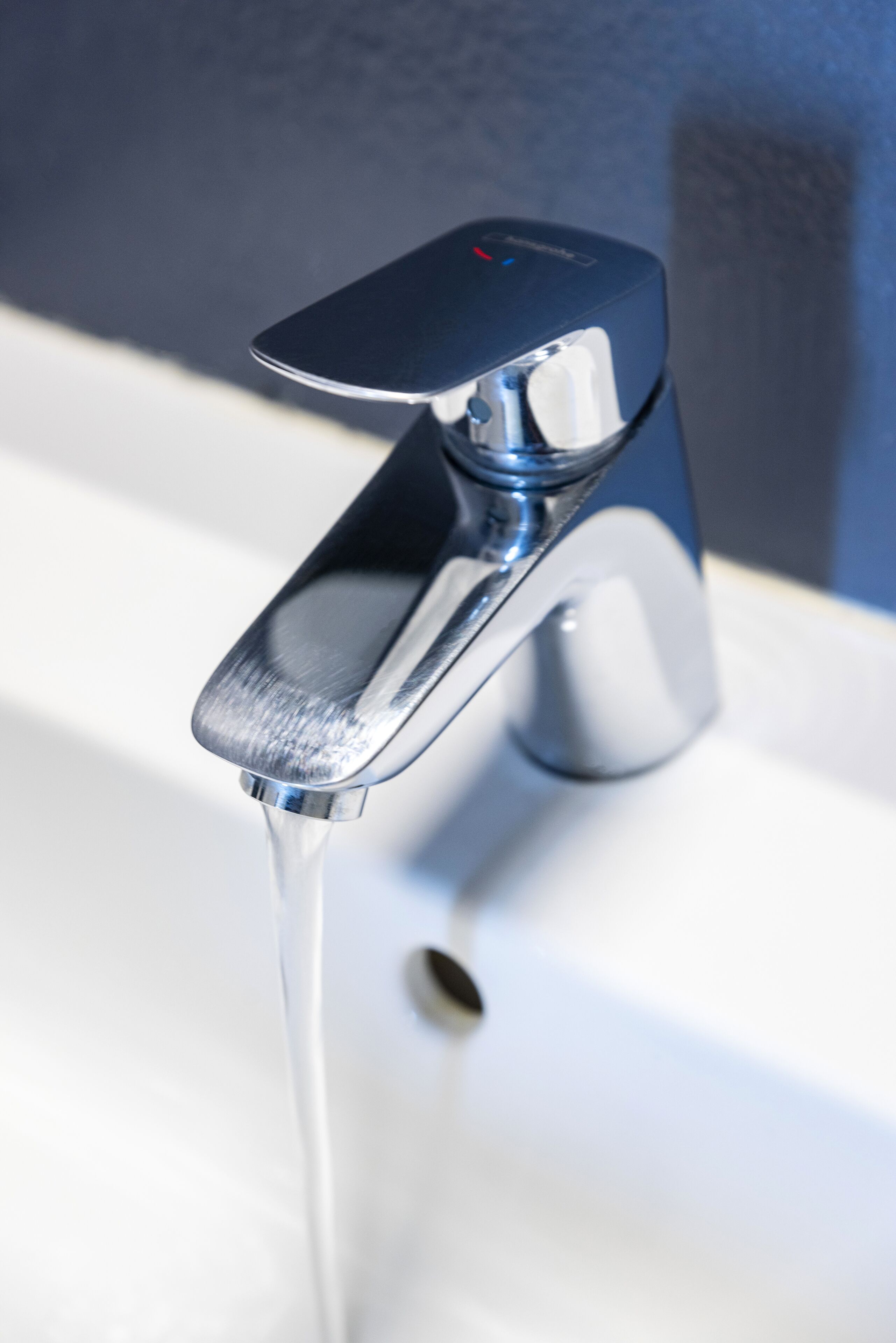 Un grifo moderno con agua corriendo, sobre un lavabo blanco frente a una pared oscura.