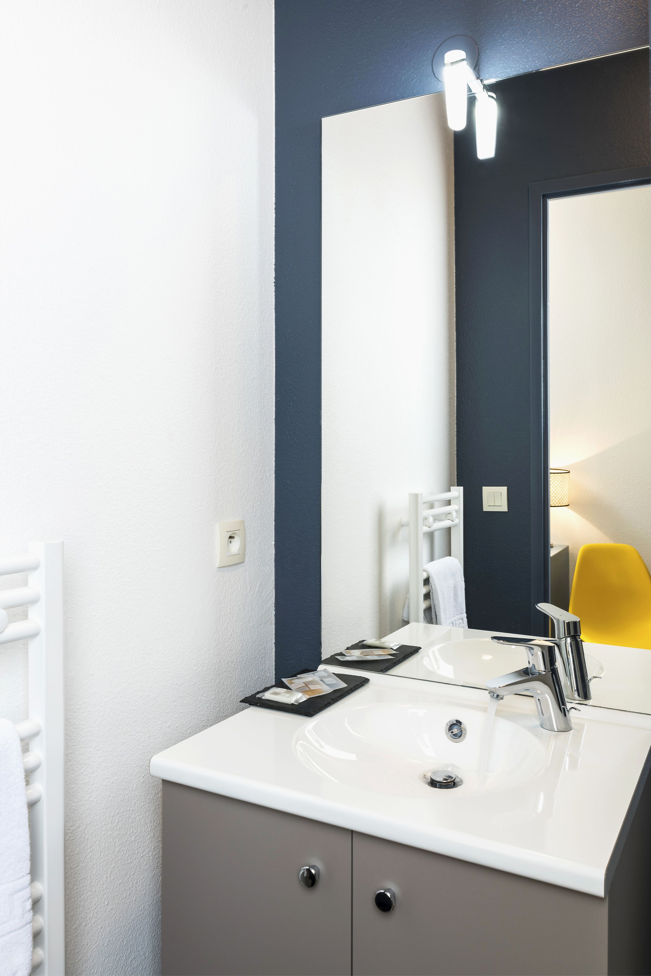 A modern bathroom with a white sink, a mirror, and a yellow chair.