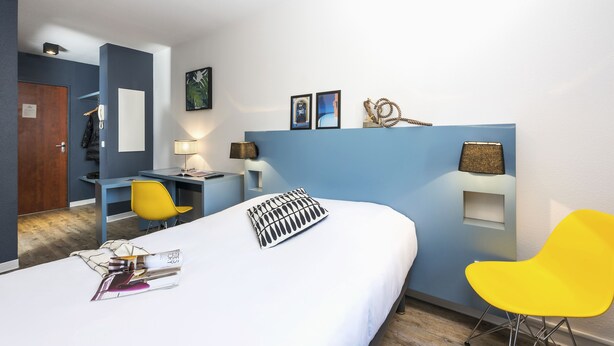 Una habitación de hotel moderna con una cama, un escritorio, una silla y una mesita.