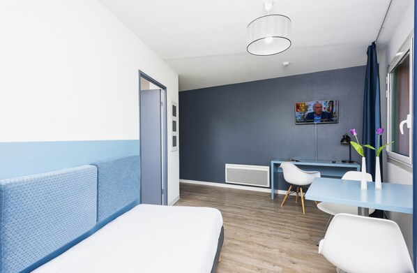 A modern hotel room with a bed, a desk, and a chair.
