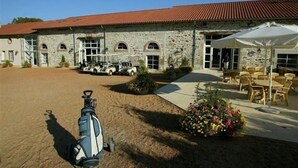 A stone building with a red roof, a covered outdoor seating area, and a golf cart parked outside. - Golf de Saint Junien (Saint-Junien)