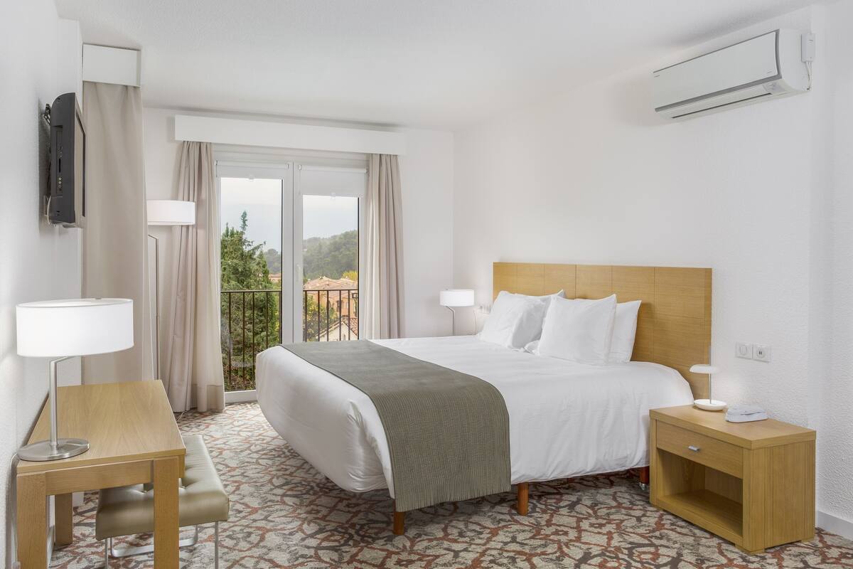 A hotel room with a bed, bedside tables, a desk, and a view of the outdoors.