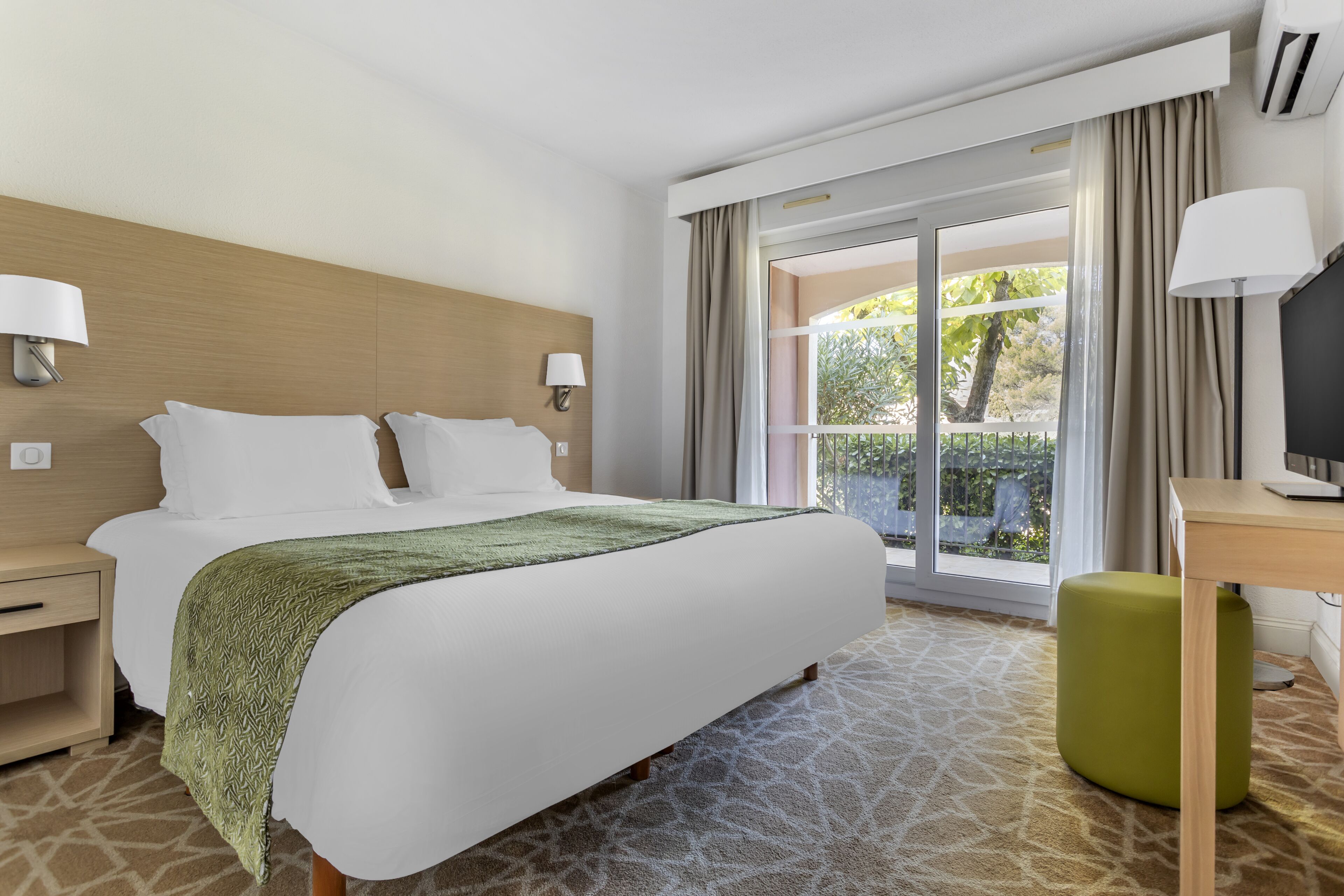 A hotel room with a bed, a desk, a television, and a view of the outdoors.