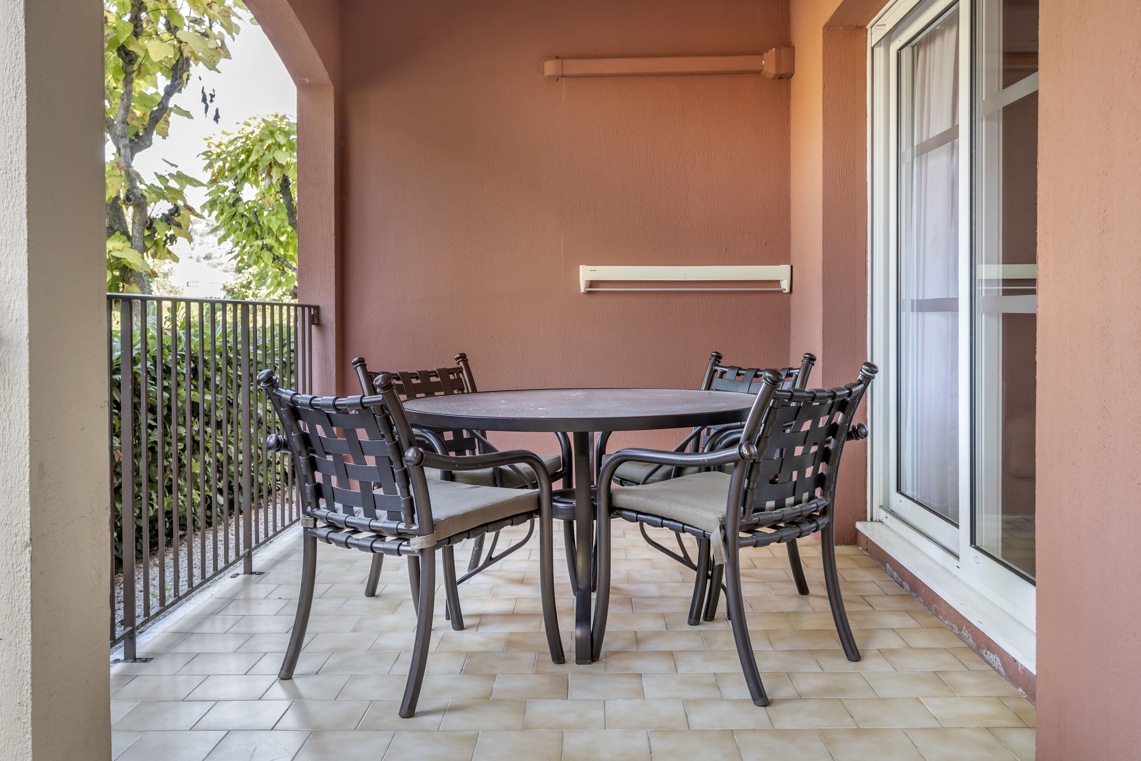 A patio with a round table and four chairs, a metal railing, and a sliding glass door.
