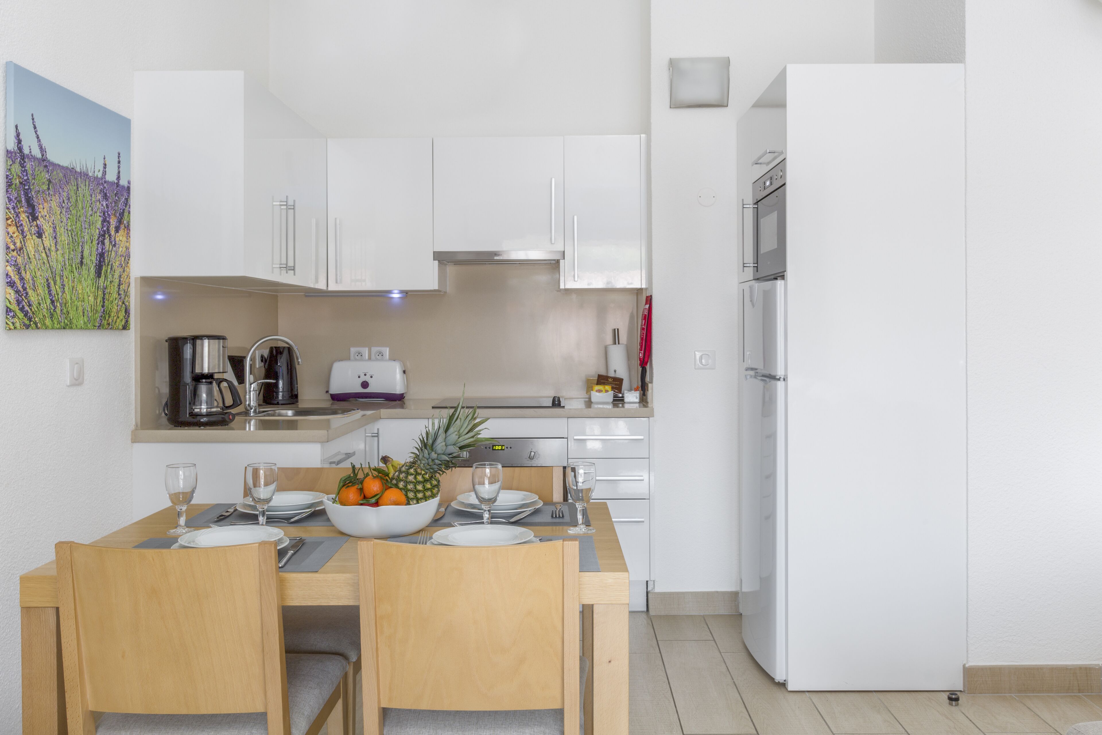 A modern kitchen with white cabinets, a dining table set for two, and a refrigerator.