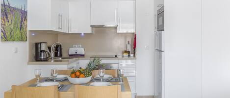 A modern kitchen with white cabinets, a dining table set for two, and a refrigerator.