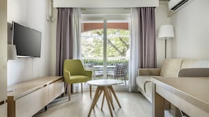 A modern hotel room with a sofa, a small round table, a TV, and a balcony with curtains. - Le Club Mougins (Mougins)