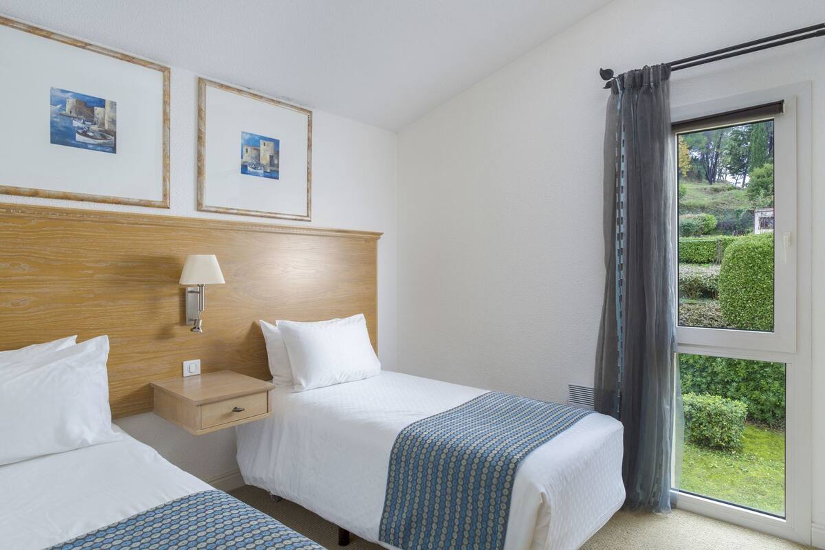 A hotel room with two beds, a wooden headboard, a nightstand with a lamp, and framed pictures on the wall.
