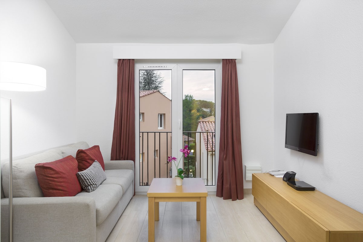 A modern living room with a sofa, a table, a TV, and a balcony with curtains.