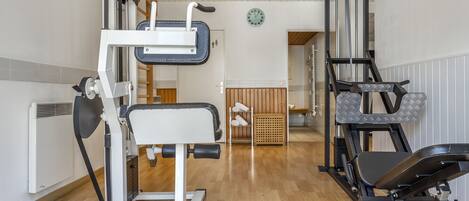 A gym with exercise equipment, wooden flooring, and a clock on the wall.