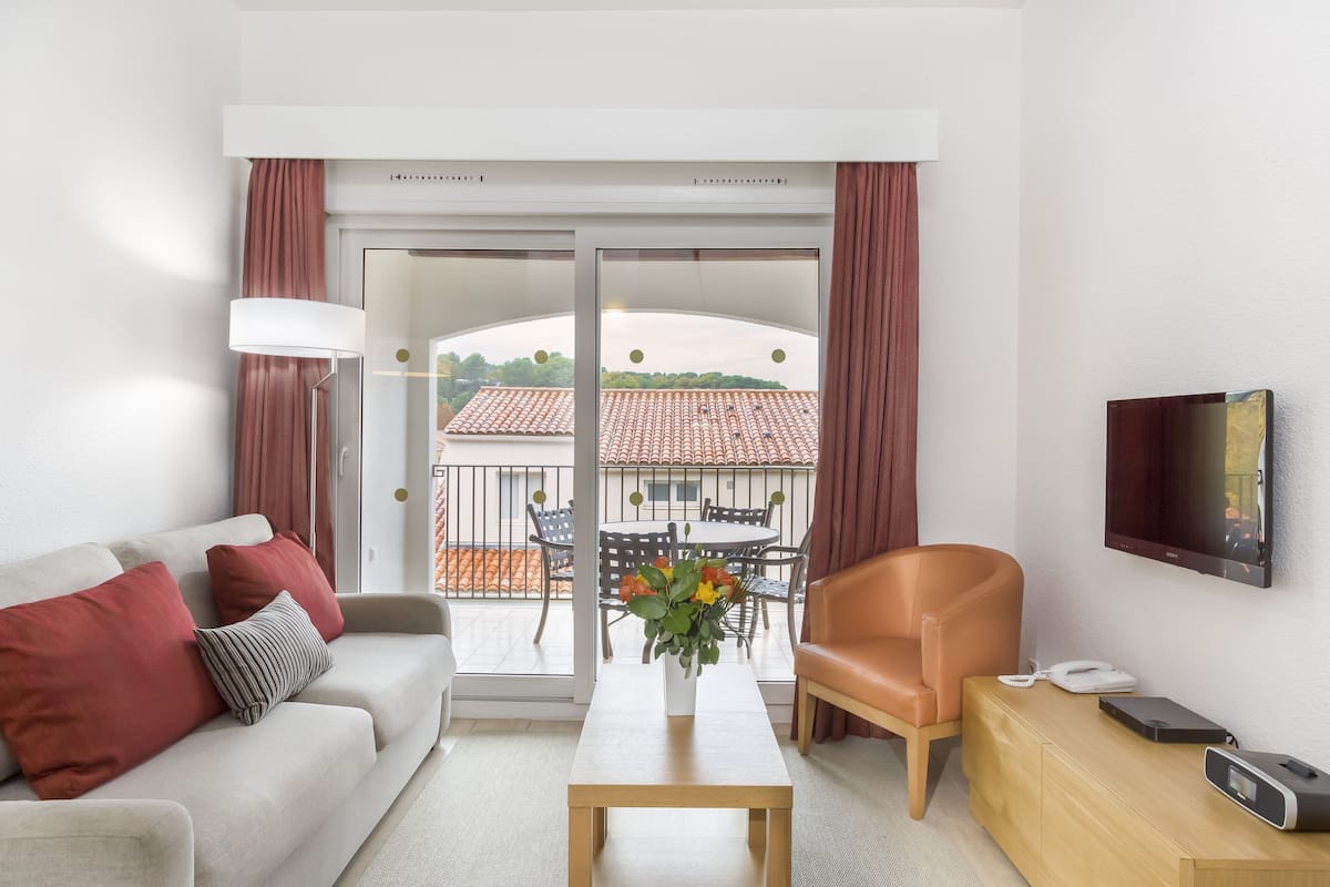 A modern living room with a sofa, a coffee table, a TV, and a balcony with outdoor furniture.