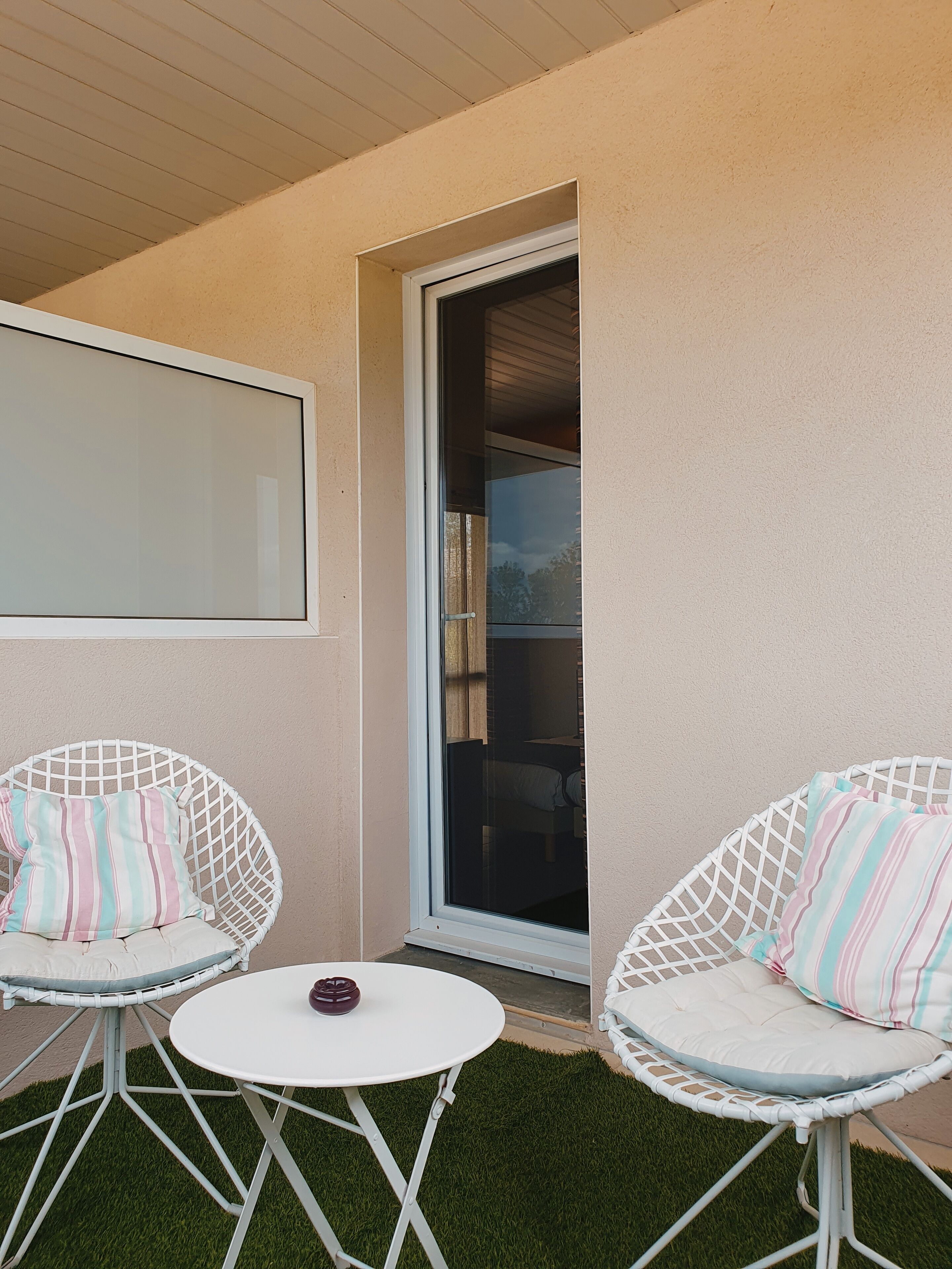 A balcony with two white wicker chairs, a small round table, and a large window.