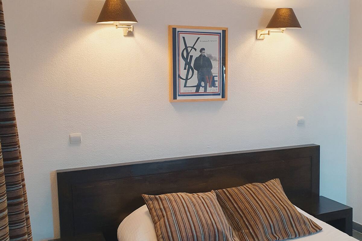 A hotel room with a bed, two bedside lamps, a framed picture on the wall, and a curtain.