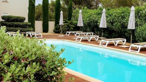 A swimming pool with lounge chairs and umbrellas, surrounded by greenery and a wooden deck. - Hôtel Le Patio de Violette (Uzès)