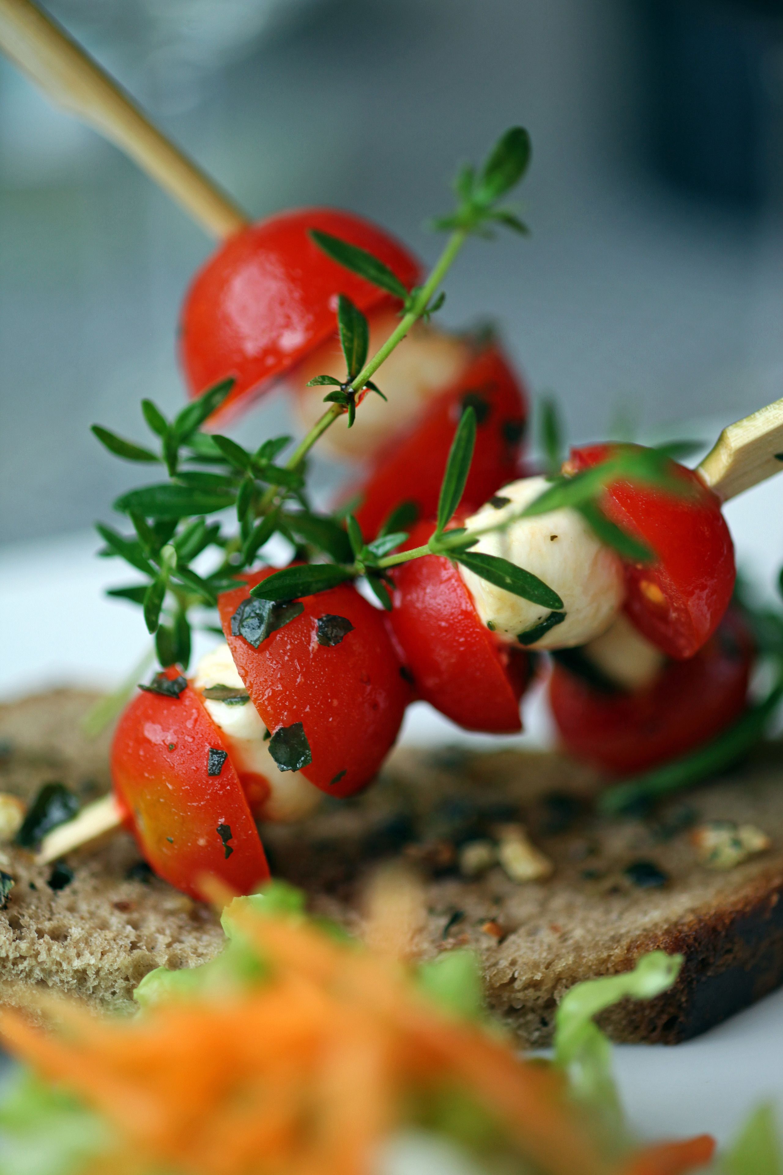 A close-up of a food item, likely a skewer with tomatoes and cheese, on a slice of bread.