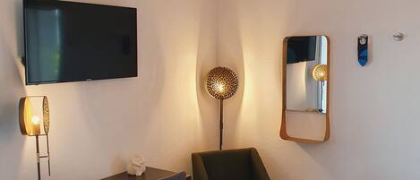 Quarto de hotel com televisão de tela plana, uma mesa com cadeira, abajur, espelho e cama.