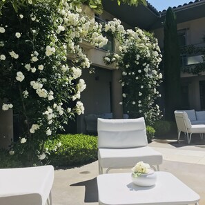 Un patio con mobiliario exterior blanco, que incluye una mesa y dos sillas, rodeado de exuberantes plantas florecientes blancas.