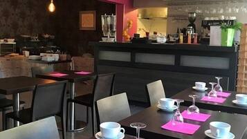 Un restaurante con mesas dispuestas para comer, una zona de bar y una cocina al fondo.