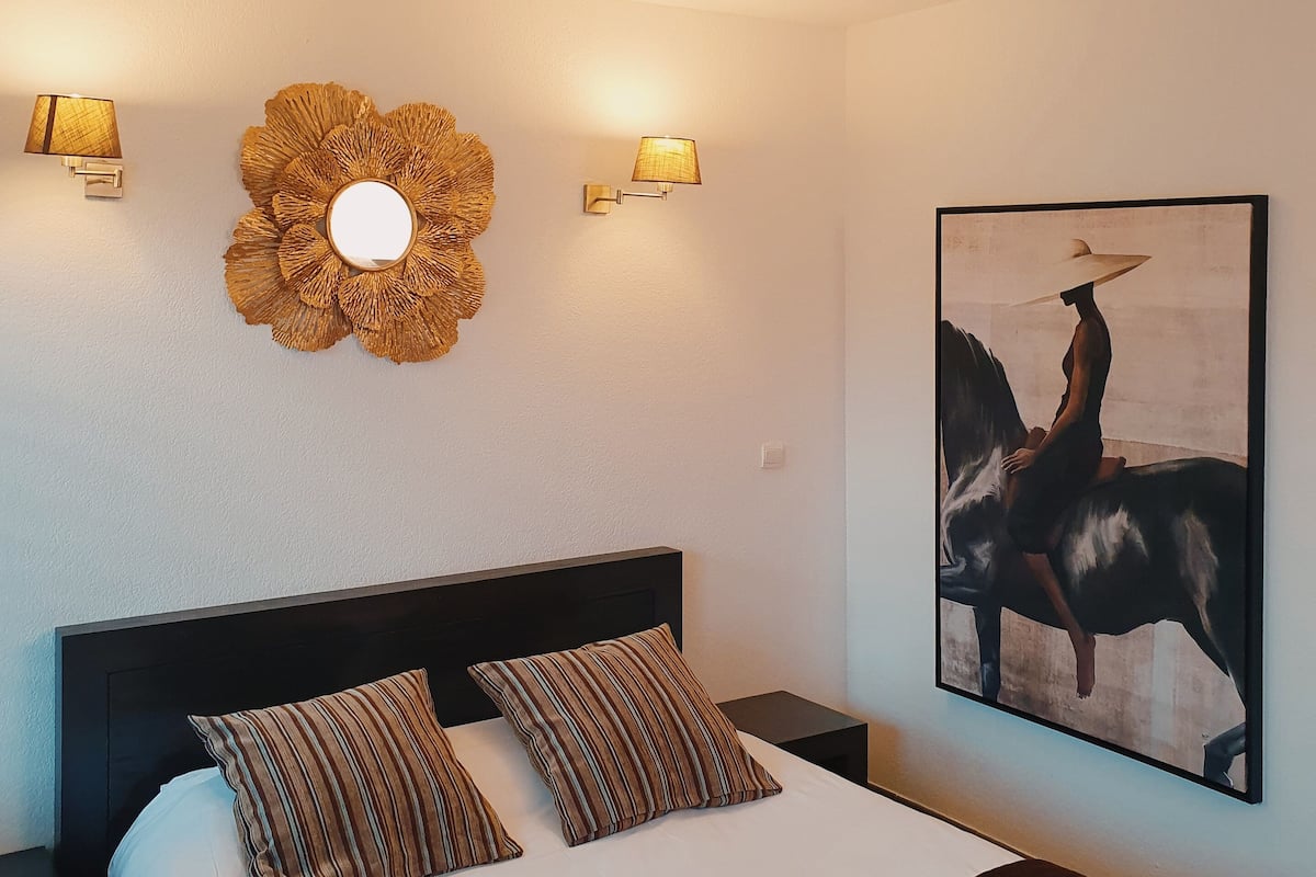 A bedroom with a bed, two wall-mounted lamps, a decorative wall piece, and a framed painting.