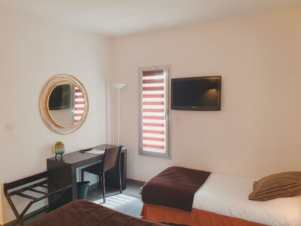Un dormitorio con cama, un escritorio con silla, un televisor montado en la pared y una ventana con persianas.