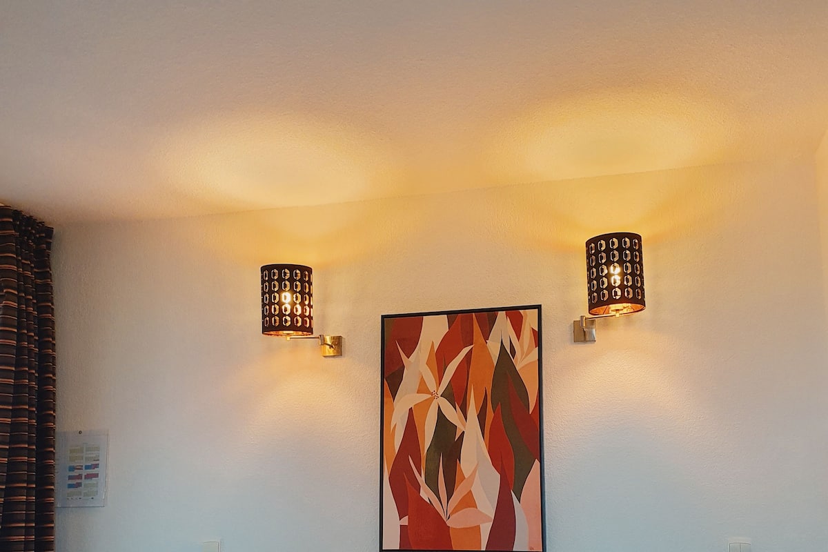 A hotel room with two beds, a large abstract painting on the wall, and two wall-mounted lamps.