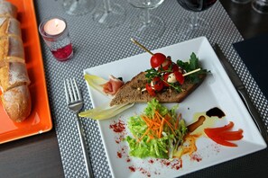 A plate with a sandwich, salad, and a small candle on a table. - Hôtel Le Patio de Violette (Uzès)