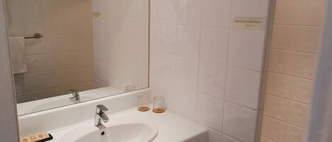 Un baño con lavamanos blanco, espejo y zona de ducha.