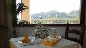 Una mesa servida con mantel blanco, una copa de vino tinto, un florero con flores y una cesta de palitos de pan.