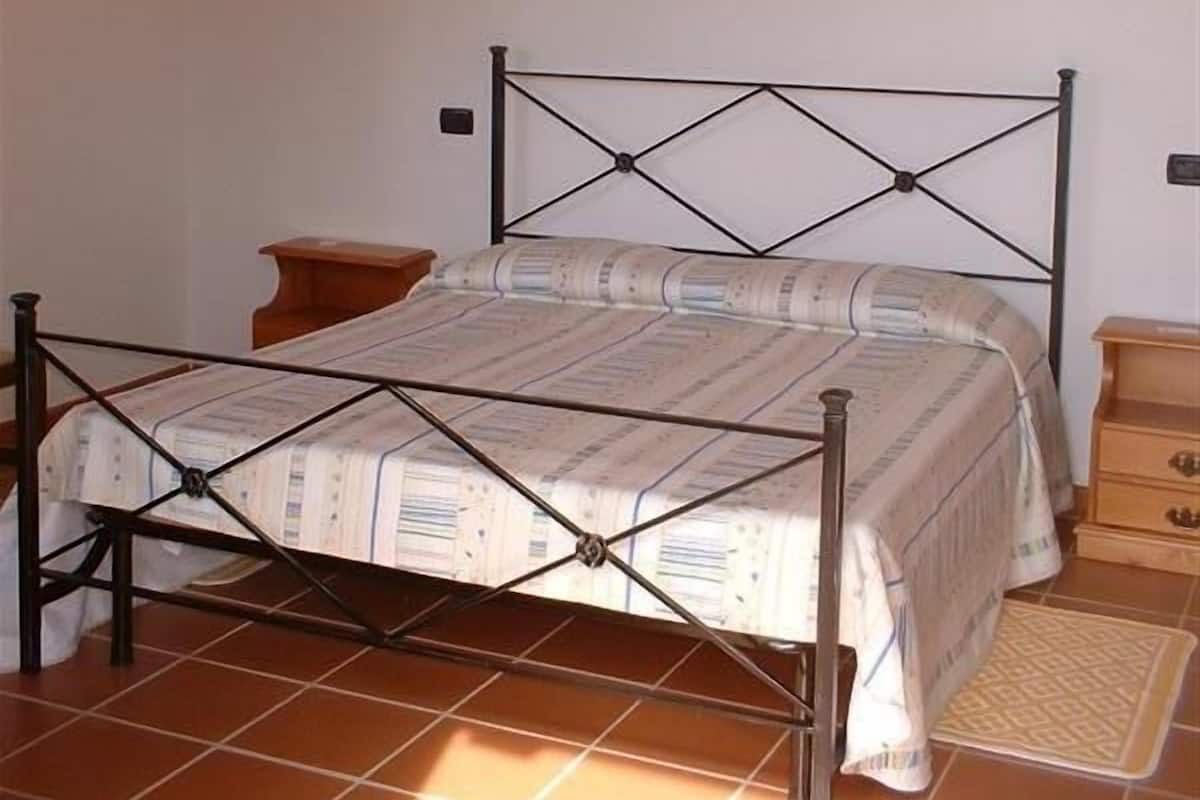 Ein Schlafzimmer mit einem Metallbettgestell, einem Holzkopfstück, einem Nachttisch und einer kleinen Holzkommode.